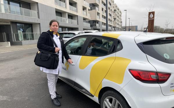 Verpleegkundige naast auto van het Wit-Gele Kruis