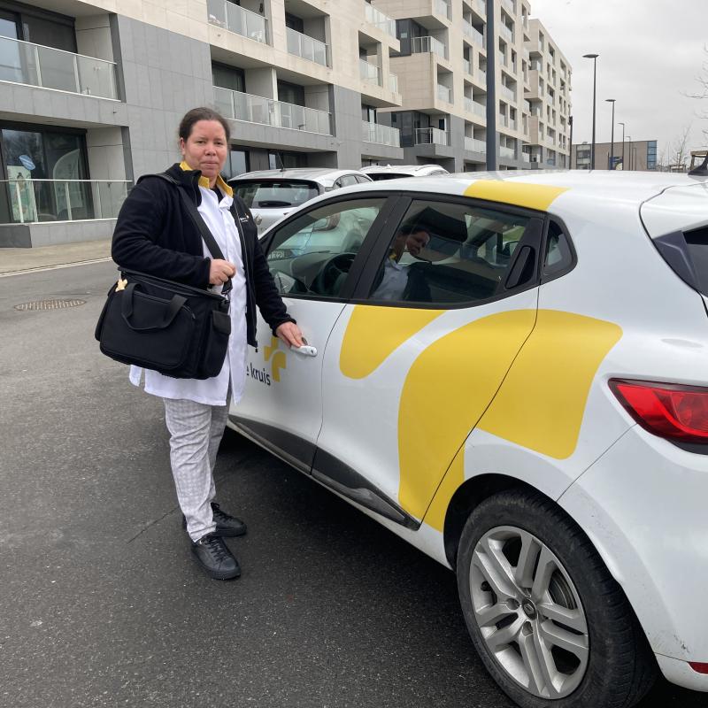 Verpleegkundige naast auto van het Wit-Gele Kruis